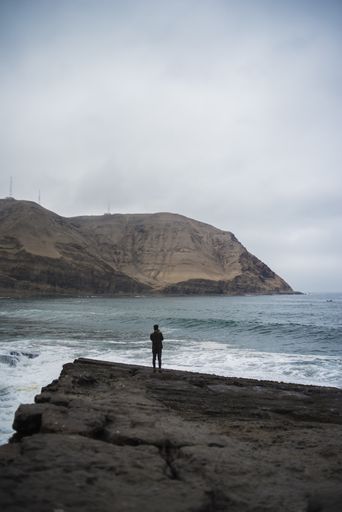 A closeup shot of a young man standing on a high rock on the beach on a cold day