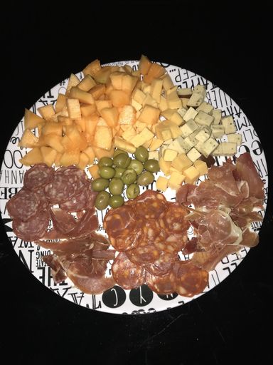 An overhead shot of sausages and cheese types and olives on a plate