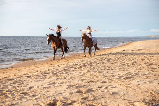 The two young female friends riding horses together on a sunny beach