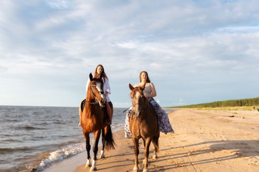 The two young female friends riding horses together on a sunny beach