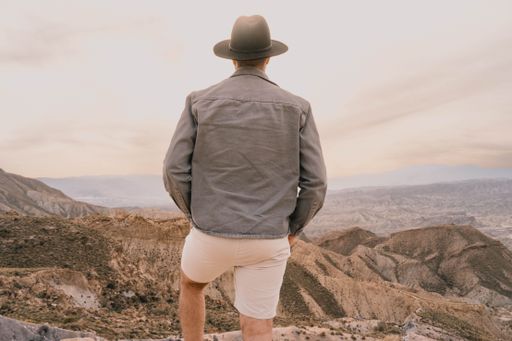 A mature man in a hat standing atop a hill at sunset