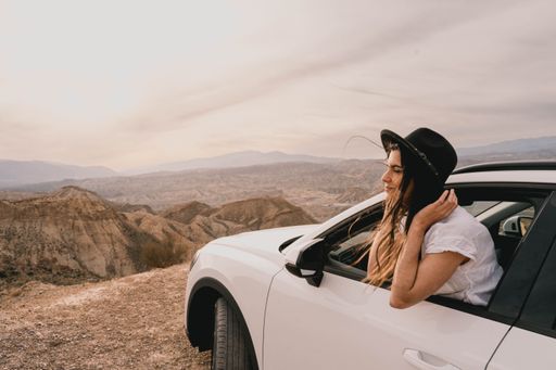 A young woman sits in a car, looking out of the window on a windy day