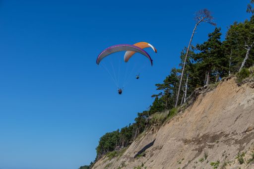 Two paragliders next to a sloping cliff.