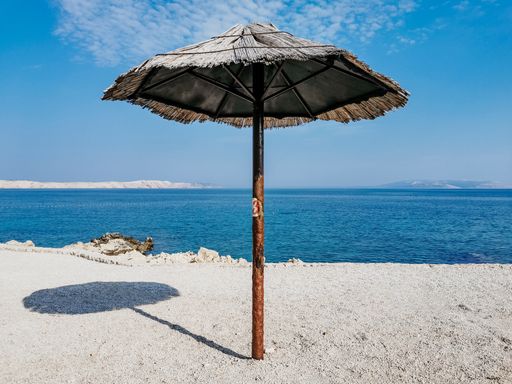 A vertical shot of an umbrella on the seashore against a blue sky background