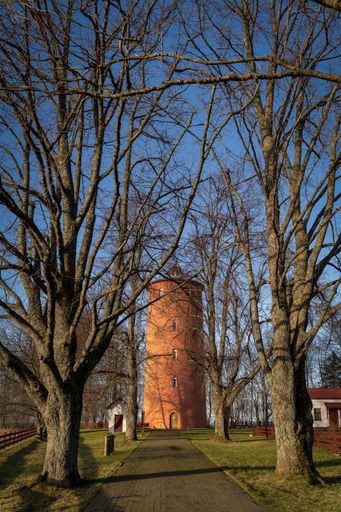 A pathway lined with bare trees leading to a brick tower under a clear blue sky