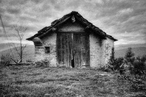 A grayscale shot of an old hut on the background of the cloudy sky