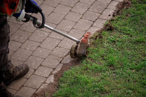 Garden maintenance worker uses an edge trimmer at the pathway.