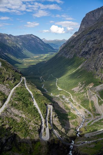 A scenic view of winding roads through a green valley in Norway, surrounded by majestic mountains