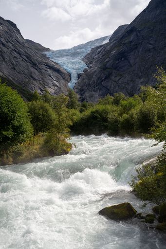 A rocky range and glacier with green trees and a river in the foreground. Briksdalsbreen, Norway