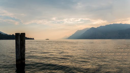 The sea surrounded by rocks under a cloudy sky and sunlight during the sunset