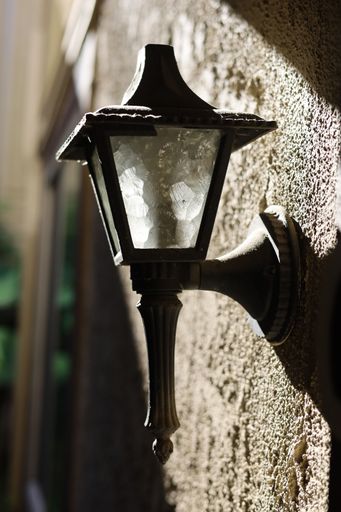 A vertical closeup of a vintage street lamp on a wall in sunlight