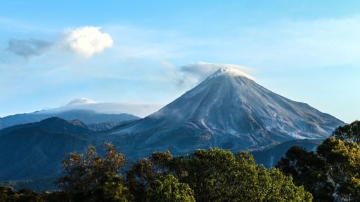 Colima's volcanoes at sunset. The iconic Volcan de Fuego gracefully exhales a plume of smoke.