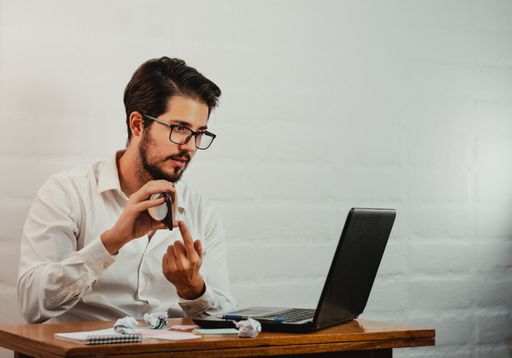 A young Caucasian male having a video call on the laptop while showing his cell phone in the office