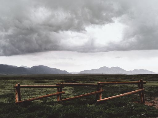 A scenic grassy landscape with a wooden split rail fence on a cloudy day