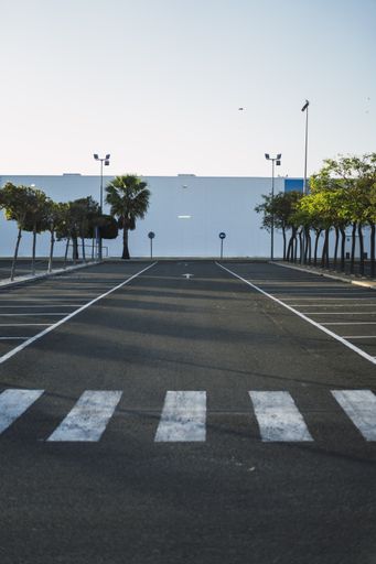 A vertical shot of an asphalt road with pedestrian lines against the clear blue sky