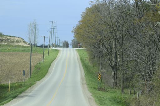 A long asphalt road surrounded by greens and trees under the blue sky