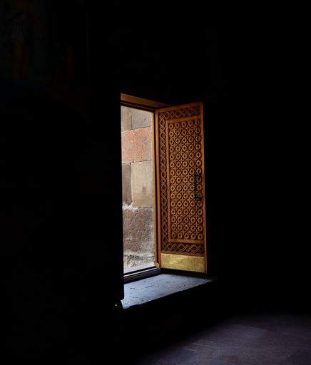 The door of the temple decorated with the wood carving shown from the dark interior space.