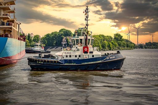 Two tugboats including the ZP Bear during the work of navigating a container ship during sunset in the harbor of Hamburg Germany