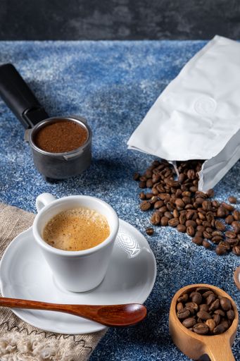 A vertical shot of a cup of coffee, a coffee container and a pile of coffee on the kitchen tabl