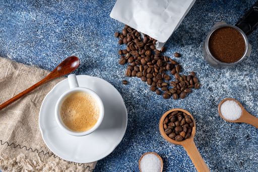 A top view of a cup of coffee, a coffee container and a pile of coffee on the kitchen table