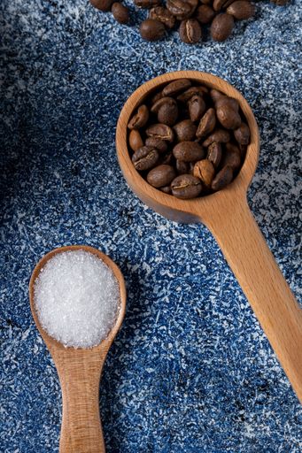 A vertical shot of a pile of coffee beans and sugar in a wooden spoon on a table