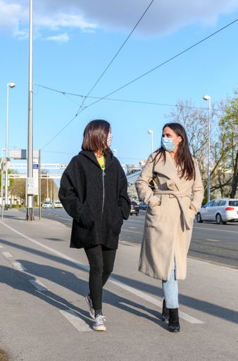 Female friends walking in city, wearing protective masks during corona virus epidemic.
