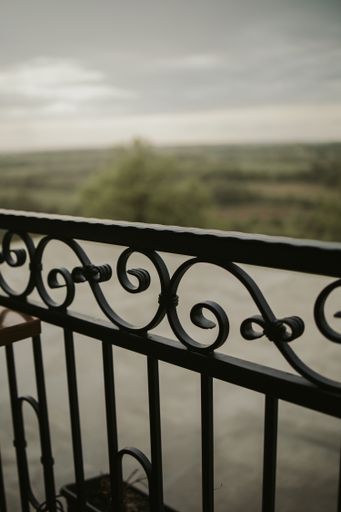 A selective focus shot of a black balcony railing with a river and forest in the blurred background