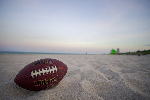 A closeup of a  rugby ball  atop a sandy beach with a blurry background