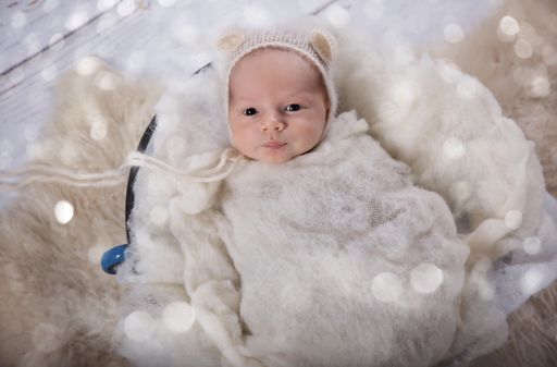 An adorable newborn Caucasian baby boy wrapped on a knitted cloth with bokeh lights