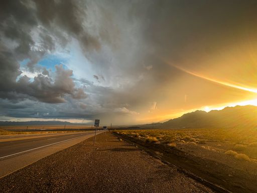 A scenic view of a highway winding through a landscape of dark storm clouds in the distance
