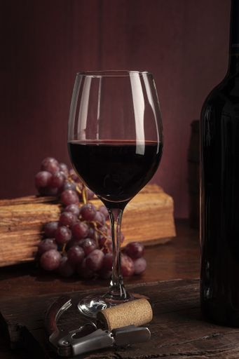 A glass of red wine near the bottle on a wooden table with grapes