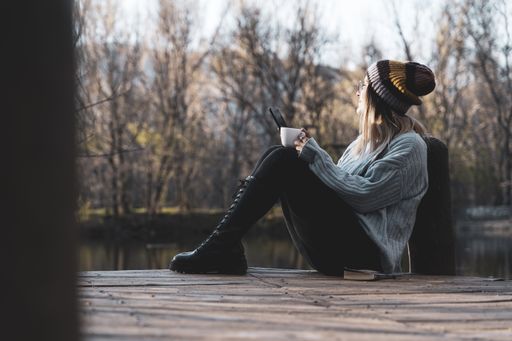 a woman relaxing on the wooden pier of the lake with a cup of coffee