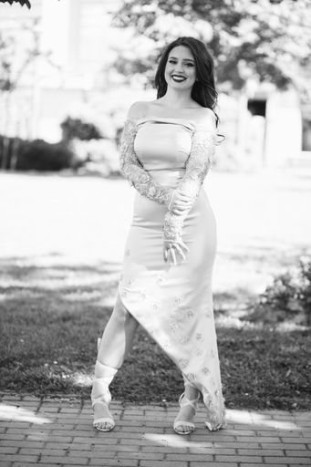 A vertical shot of a smiling Caucasian female with beautiful dress posing outdoors