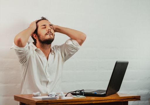A young Caucasian male gesturing fatigue and stress by holding head with hands, taking a deep breath