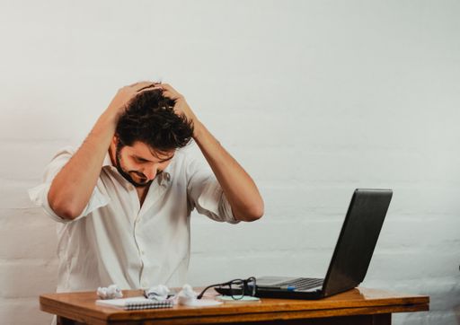 A young Caucasian male gesturing fatigue and stress by holding head with hands, taking a deep breath
