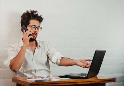 A young Caucasian male looking at the laptop and gesturing while having a phone call in the office