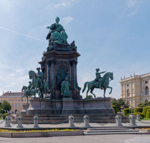 An artistic sculpture of multiple riders on horseback situated in front of a large building, illuminated by the sun