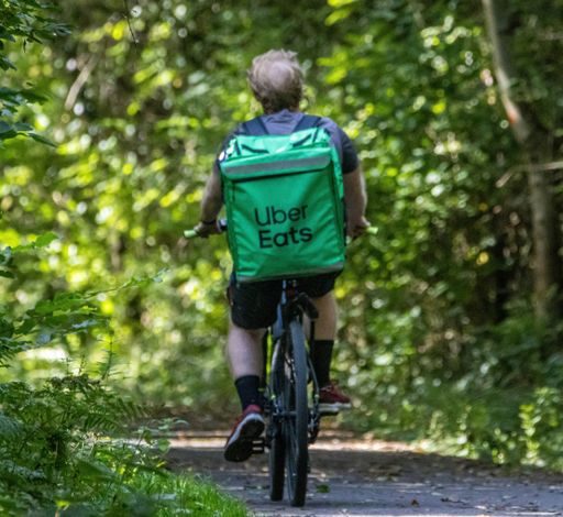 A male riding his bicycle in the forest, looking back over his shoulder: Uber Eats
