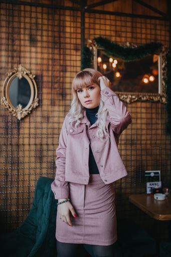 An attractive Caucasian female wearing a black turtleneck shirt and a pink jacket