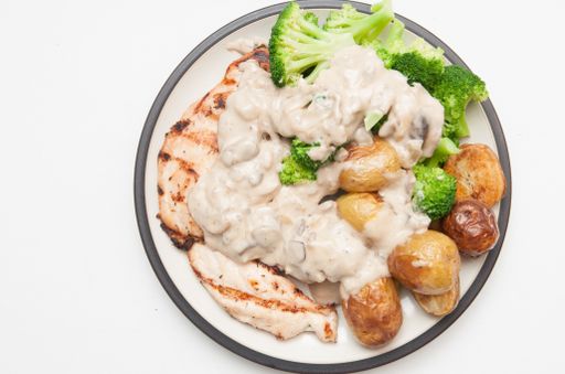 A top view of cooked meat or fish with potatoes, broccoli and white sauce on a plate isolated on a white surface
