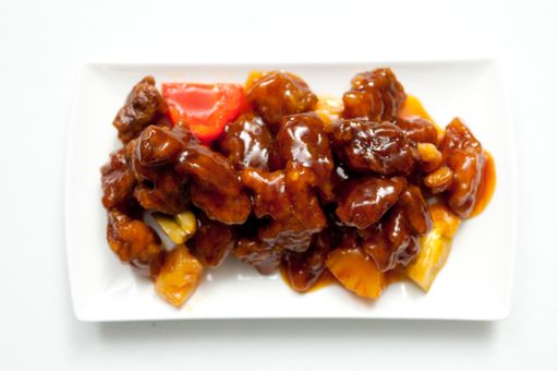 a top view of Chinese chicken with red sauce and pepper slices on a white plate isolated on a white surface
