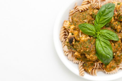 A top view of pasta with sauce in a white plate decorated with basil leaves isolated on a white background