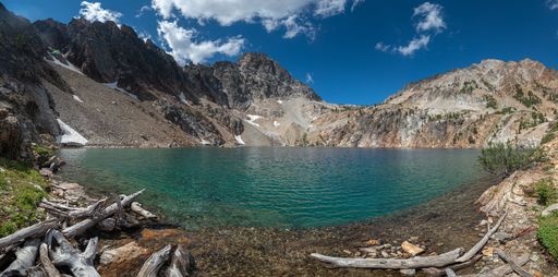 A tranquil mountain landscape featuring a calm lake nestled between large fallen tree trunks