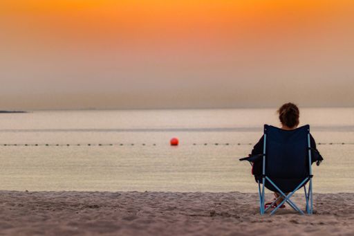 A woman sitting on a portable chair on the sandy beach and admiring the amazing views of the sunset