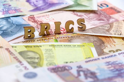 A closeup of a stack of various currency banknotes with the letters BRICS on top