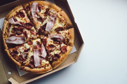 A high angle view of a pizza with bacon cut in slices in a box on the table under the lights
