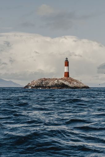 A vertical shot of a lighthouse on an island on a cloudy day