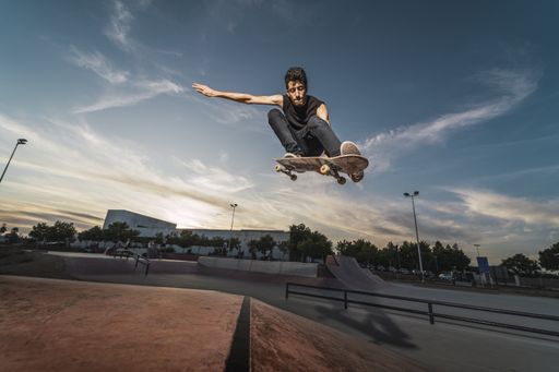 A low angle shot of a Caucasian athletic male in a black outfit doing a flip trick with a skateboard