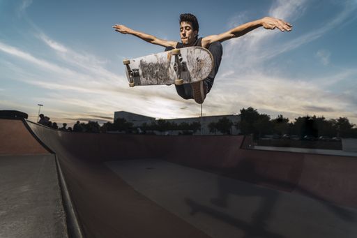 A low angle shot of a Caucasian athletic male in a black outfit doing a flip trick with a skateboard