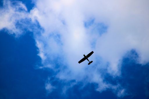 A low angle of an old airplane flying under a cloudy blue sky